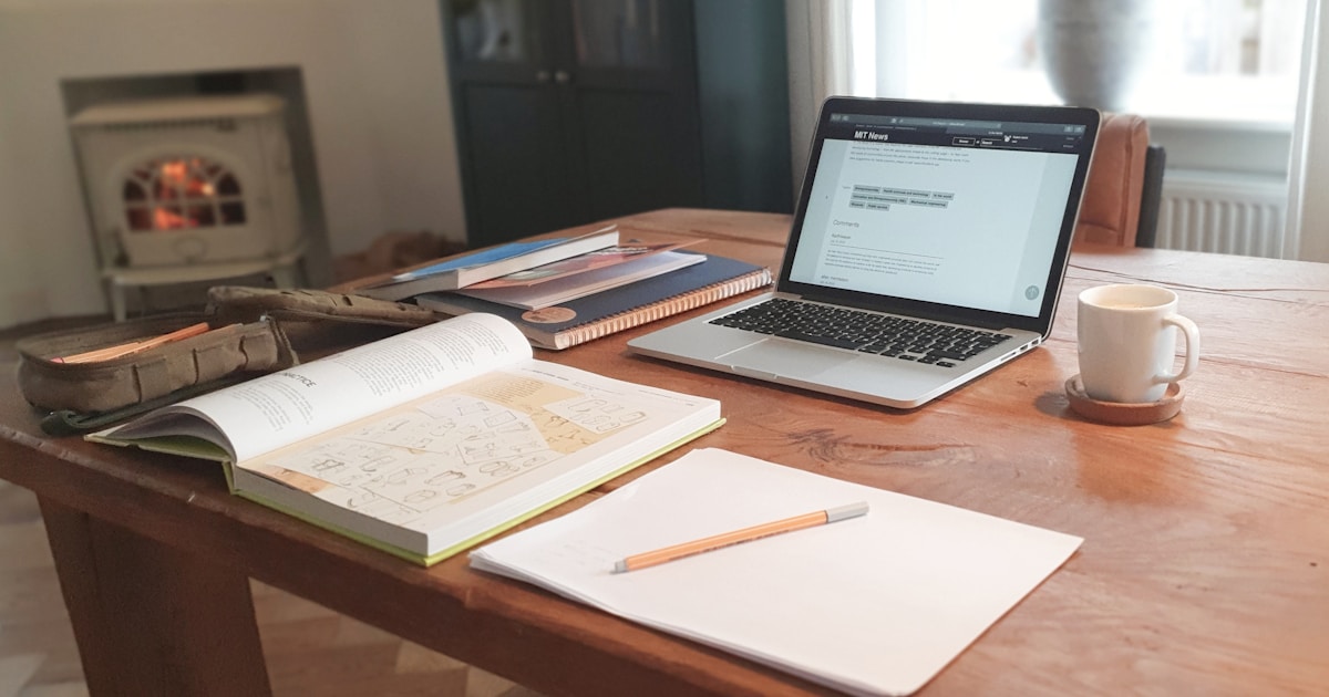 Warm wooden desk with open reference book, laptop, notepad, and coffee mug, representing a therapist reviewing CAP practice standards
