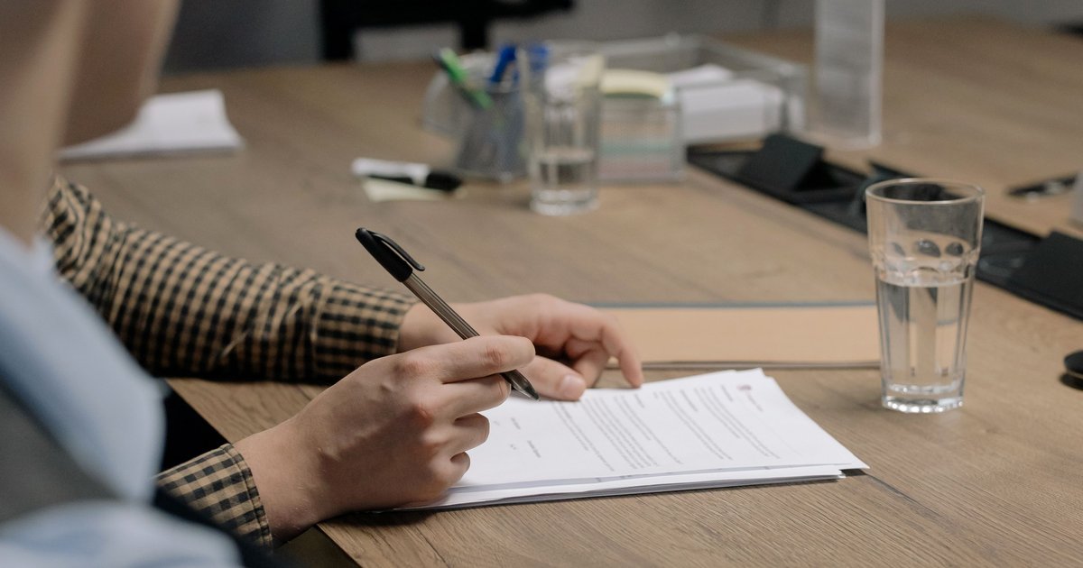 A hand signing a paper contract with a pen at a wooden office desk, representing a Canadian therapist reviewing what a Google Workspace BAA actually covers