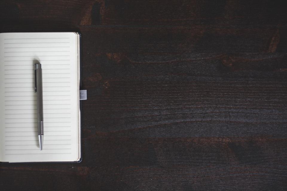 Open notebook and pen on a dark wood desk, the working surface for a practice privacy checklist